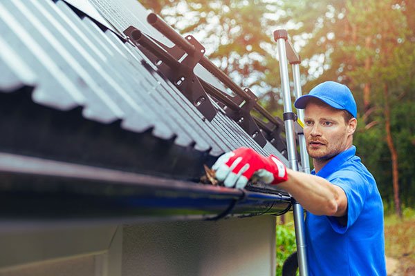 Tradesman cleaning roof guttering to prevent blockages