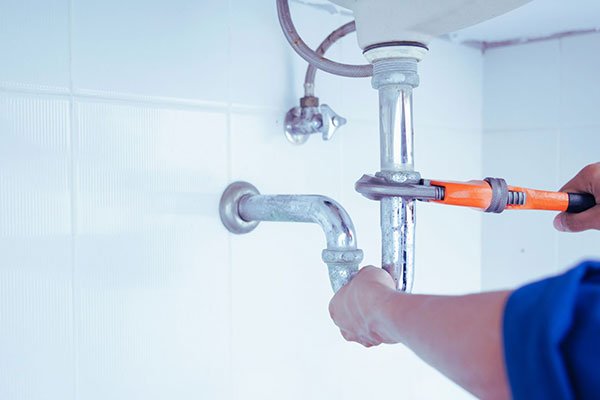 Plumber repairing under-sink pipework with adjustable wrench
